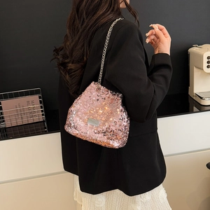Pink sequin crossbody bag with gold chain strap shown on model in a modern interior
