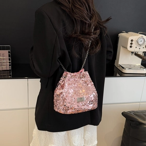Close-up of pink sequin bucket bag with silver chain strap worn by a model