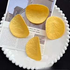 Detail shot of four yellow potato chip hair clips on a white plate with aesthetic cards