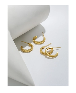 Detailed view of four golden C-shaped beaded stud earrings on white geometric stands