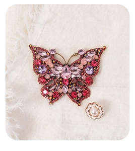 Close-up of luxury butterfly brooch with pink crystals and small white enamel flower pin