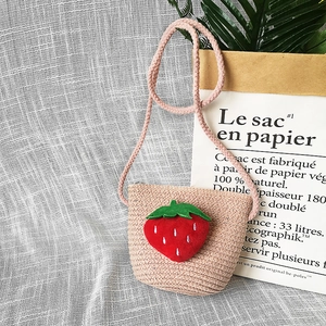 Detail view of pink straw crossbody bag for kids with cute plush strawberry decoration