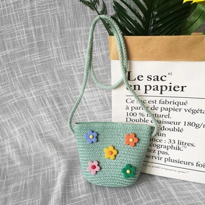 Detail of light green straw crossbody bag with colorful floral decorations and braided strap