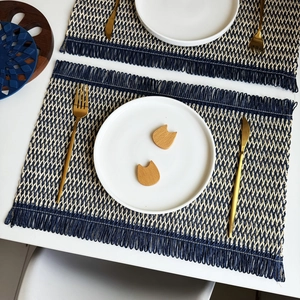 Detail of woven placemat with navy herringbone pattern and decorative fringe edges