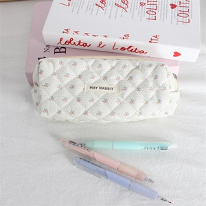 Close-up view of a floral quilted cosmetic bag with books and pastel pens on a white cloth
