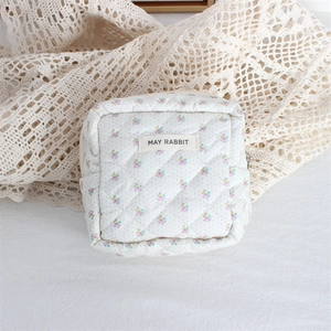 Detailed view of quilted floral cosmetic bag with May Rabbit label on white lace