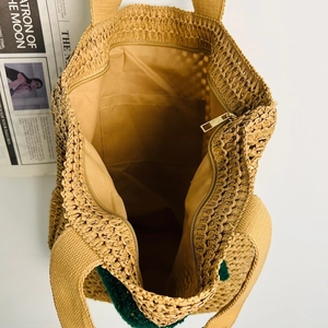 Detail view of khaki straw tote bag featuring zipper closure and internal pocket lining