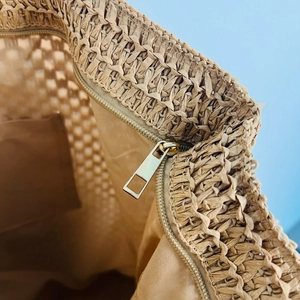 Detail of straw tote bag interior featuring fabric lining and golden metal zipper
