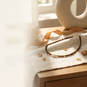 Detail of tiger eye bead necklace with baroque pearl on linen fabric in warm natural light