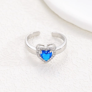Detail of an open heart ring with a blue gemstone center and white zircon stones