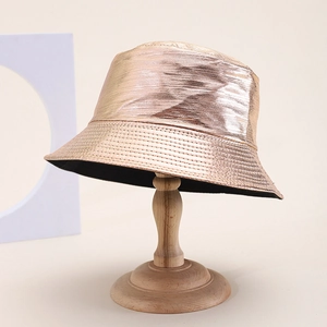 Metallic rose gold PU leather bucket hat with wide brim on a wooden display stand