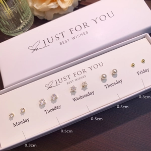 Detail of five pairs of assorted stud earrings in a white gift box with weekday labels