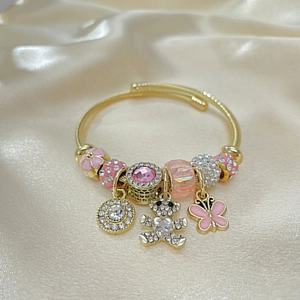 Detail of gold charm bracelet with pavé bear and pink enamel flower on silk fabric