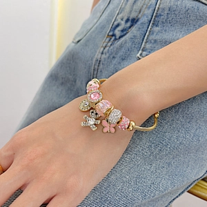 Golden open cable bracelet with pink charms and sparkling bear pendant on wrist