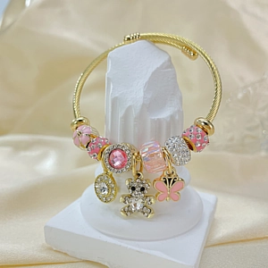Detail of a gold twisted wire bracelet with pink enamel beads and a pavé bear charm