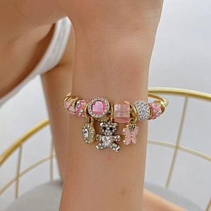 Detailed close-up of a gold steel bracelet featuring pink bear and butterfly charms