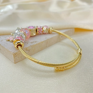Detail of gold twisted bangle with pink enamel charms and shimmering crystal beads