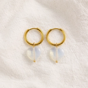 Close-up of 18K gold hoop earrings with white translucent heart-shaped stone pendants