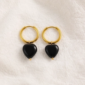 Detail of 18K gold earrings with black heart-shaped natural stone pendants on white linen