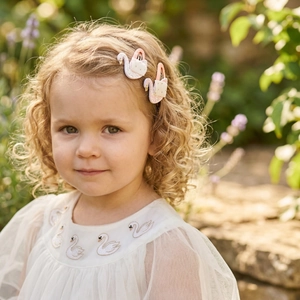 Close-up of sparkling swan hair clips and white tulle dress with swan embroidery on a girl