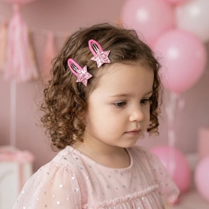 Close-up of a young girl wearing cute pink sequin star hair clips with a festive background