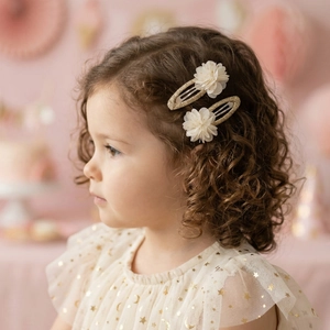 Close-up of a child wearing golden glitter hair clips with cream tulle flower details