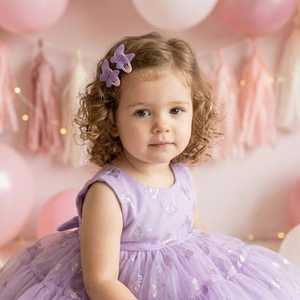 Toddler girl in purple mesh party dress with butterfly clips and festive balloon decor