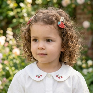 Close-up of a young girl wearing a cute red glitter strawberry hair clip with matching embroidery