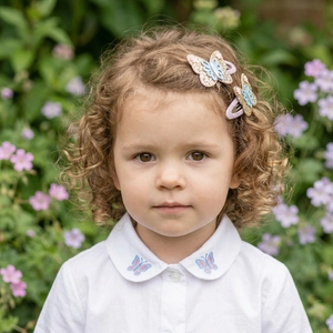 Detail of sequined butterfly hair clips in purple and gold on a young girl in a garden