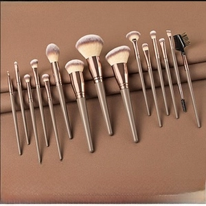 Flat lay of 15 mini makeup brushes with brown-white gradient bristles on brown fabric
