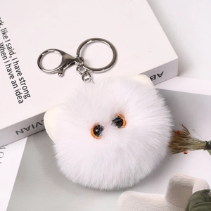 Close-up of a white fluffy monster keychain with big orange eyes on a book