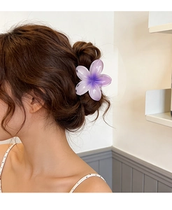 Detail view of a purple gradient plumeria hair claw clip worn on a messy bun hairstyle