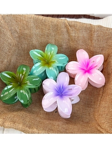 Detail of four colorful frangipani hair claws with gradient petals in a woven basket