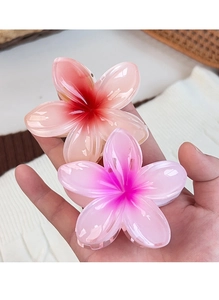 Close-up of gradient plumeria hair claws in pink and orange resin held by hand