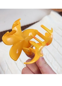 Detail of yellow flower hair claw clip with metal spring held against a white sweater