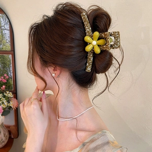 Large floral hair claw clip with yellow flower, worn in a stylish updo