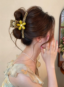 Detail view of large forest style flower hair claw clip worn on model's bun