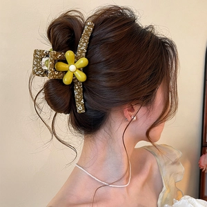 Close-up of olive floral hair claw clip with yellow flower decoration on brown hair bun.