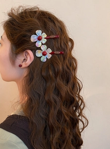 Close-up of iridescent resin flower hair clips with red beads worn on wavy brown hair