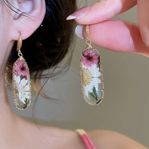 Dettaglio di orecchini in resina in stile pastorale con vere fiori secchi rosa e bianchi