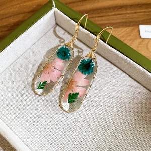 Dettaglio di orecchini in resina fatti a mano con veri fiori secchi rosa e verde