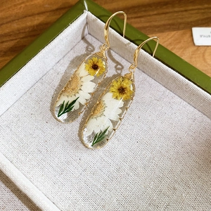 Dettaglio degli orecchini in resina con fiori secchi gialli e bianchi stile pastorale