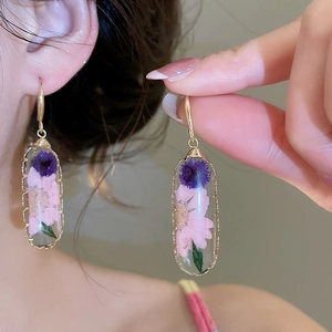 Dettaglio di orecchini in resina fatti a mano con veri fiori secchi viola e rosa.