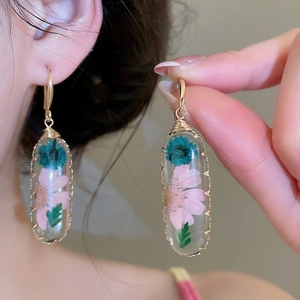 Dettaglio di orecchini in resina con veri fiori secchi rosa e blu con ganci dorati