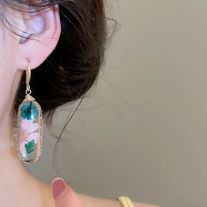 Primo piano di un elegante orecchino a goccia con veri fiori secchi rosa e verdi