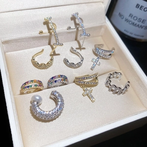 Close-up of various sparkling zircon ear cuffs with cross and pearl details in a jewelry box.
