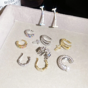Detailed view of sparkling zircon-encrusted ear cuffs in various shapes on a gray tray.