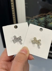 Detailed view of elegant gold and silver bow ear clips held on white display cards.