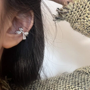 Detailed view of a sparkling silver bow-shaped ear cuff with zircons worn on a model's ear