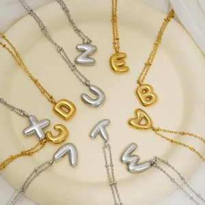 Detail view of gold and silver bubble letter necklaces on a ceramic plate with bead chains